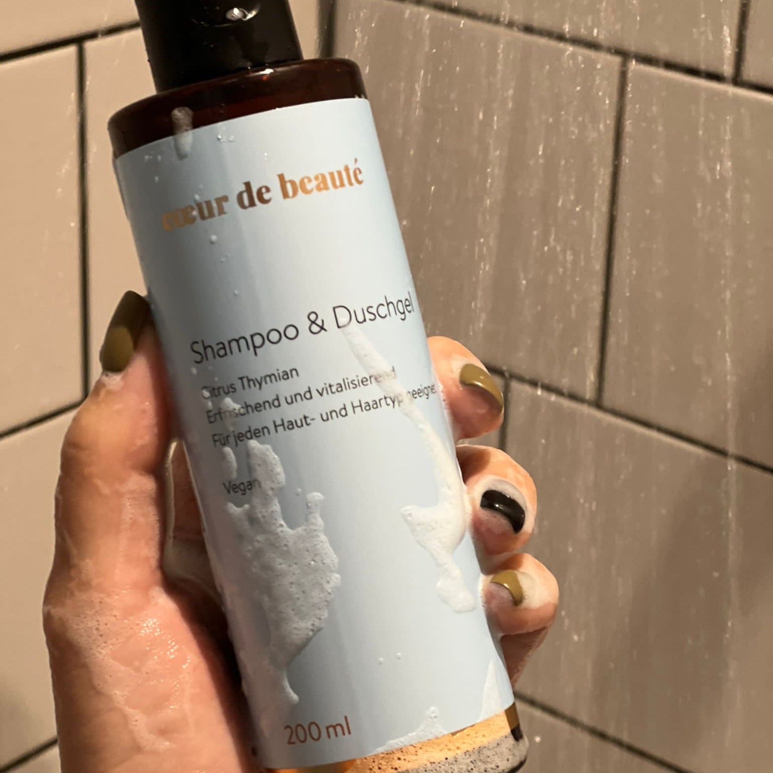 Hand in der Dusche hält das Shampoo & Duschgel von cœur de beauté.