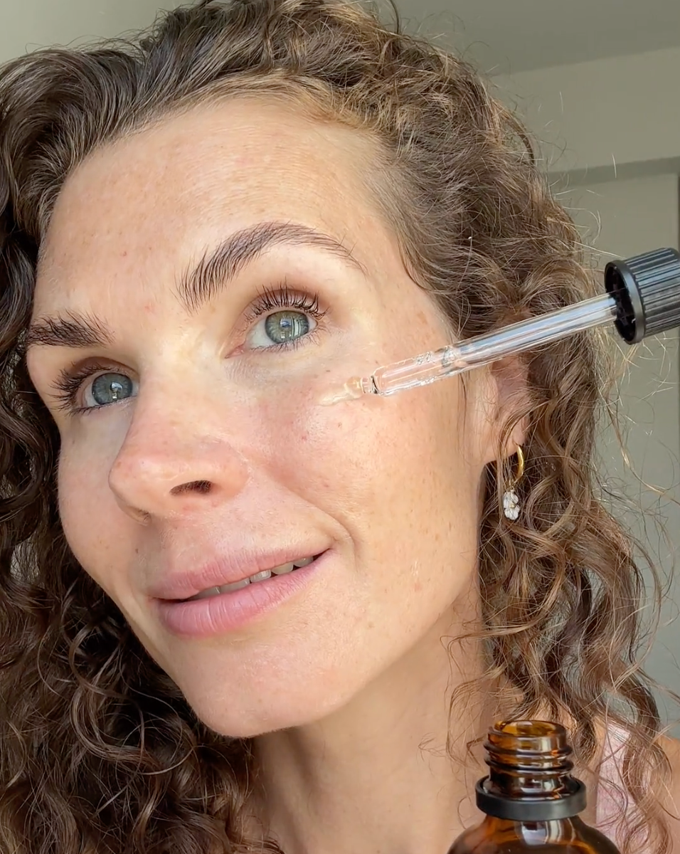 Frau hält eine Pipette mit Serum von cœur de beauté nahe des Gesichts.