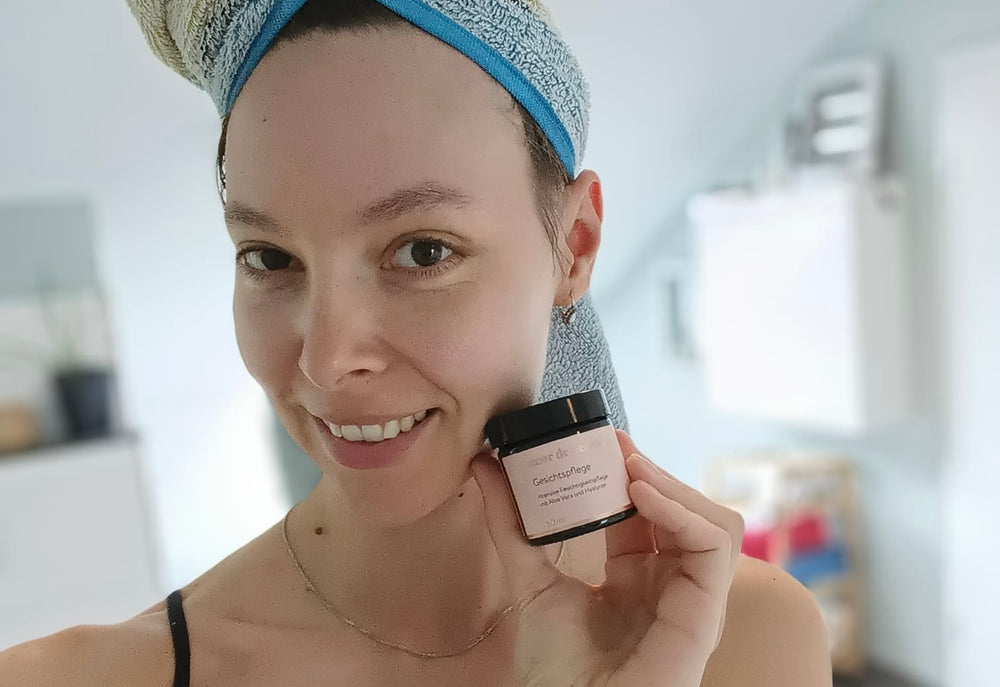 Frau hält einen Gesichtspflege-Tiegel von cœur de beauté nahe ihres Gesichts.