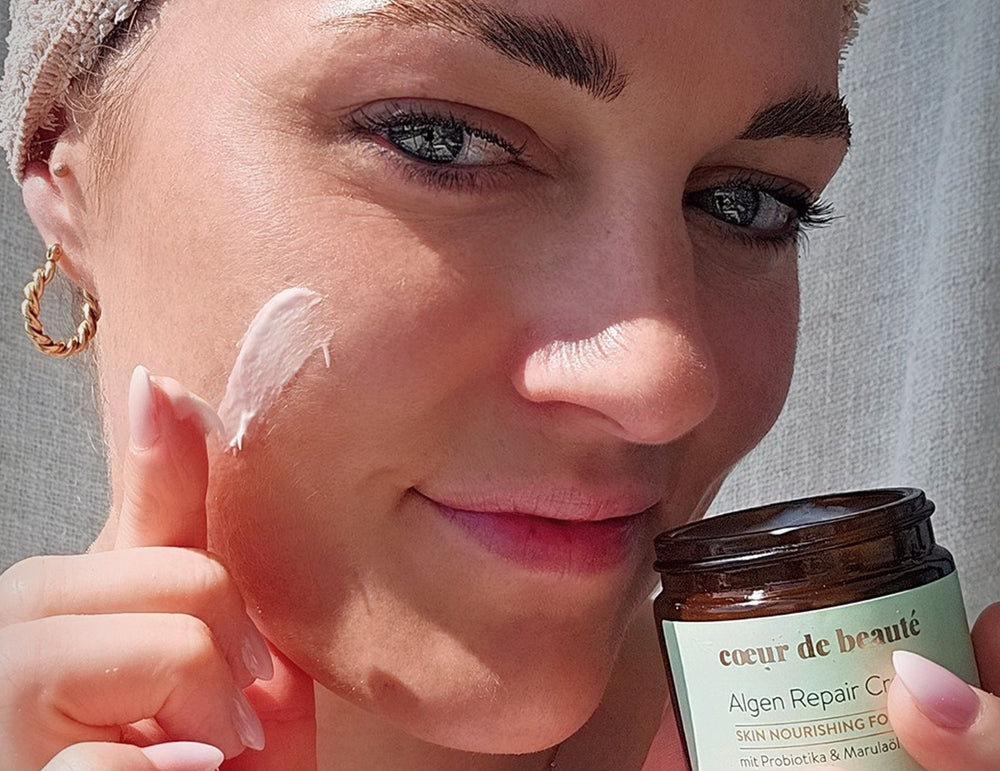 Frau hält Algen Repair Creme -Tiegel von cœur de beauté nahe ihres Gesichts.