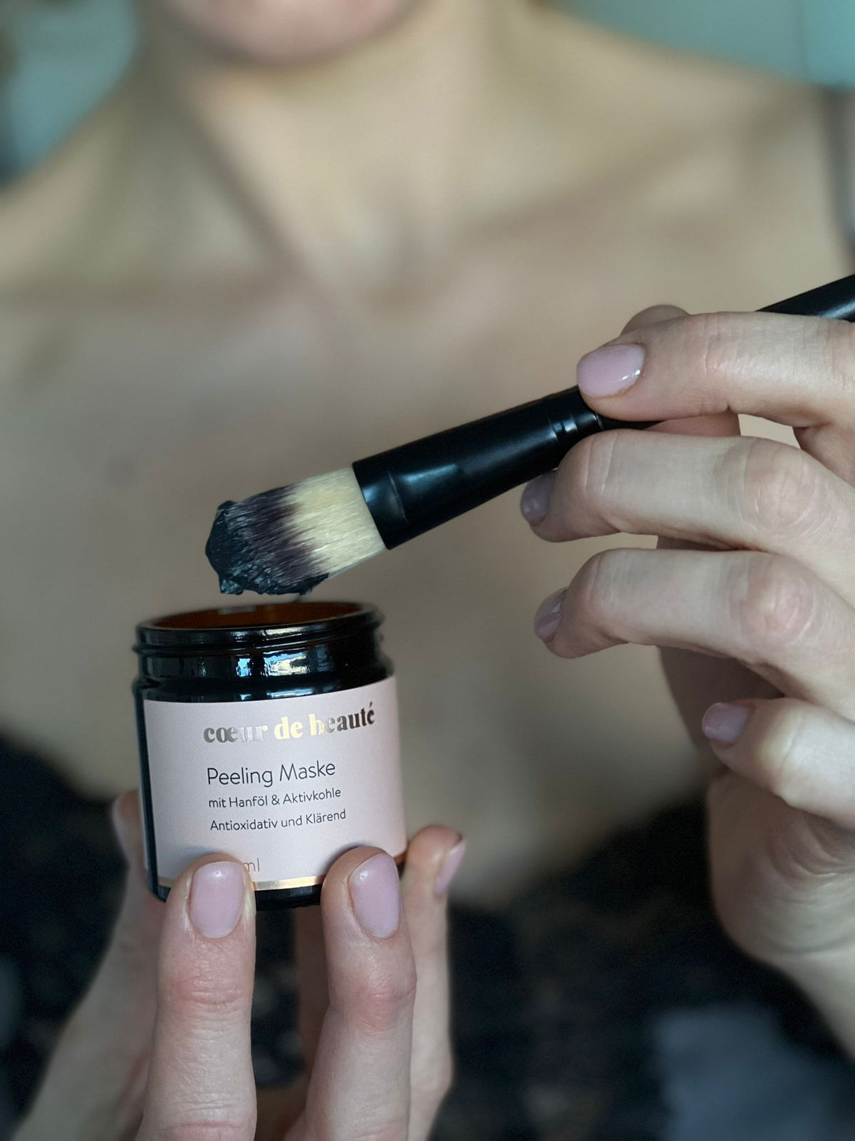 Hand Frau mit aufgetragener schwarzer Peeling-Maske im Gesicht.
