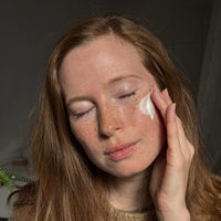 langhaarige Frau mit rötlichen haaren die eine Creme von coeur de beaute aus Berlin in gesicht aufträgt und die augen dabei geschlossen hat. 