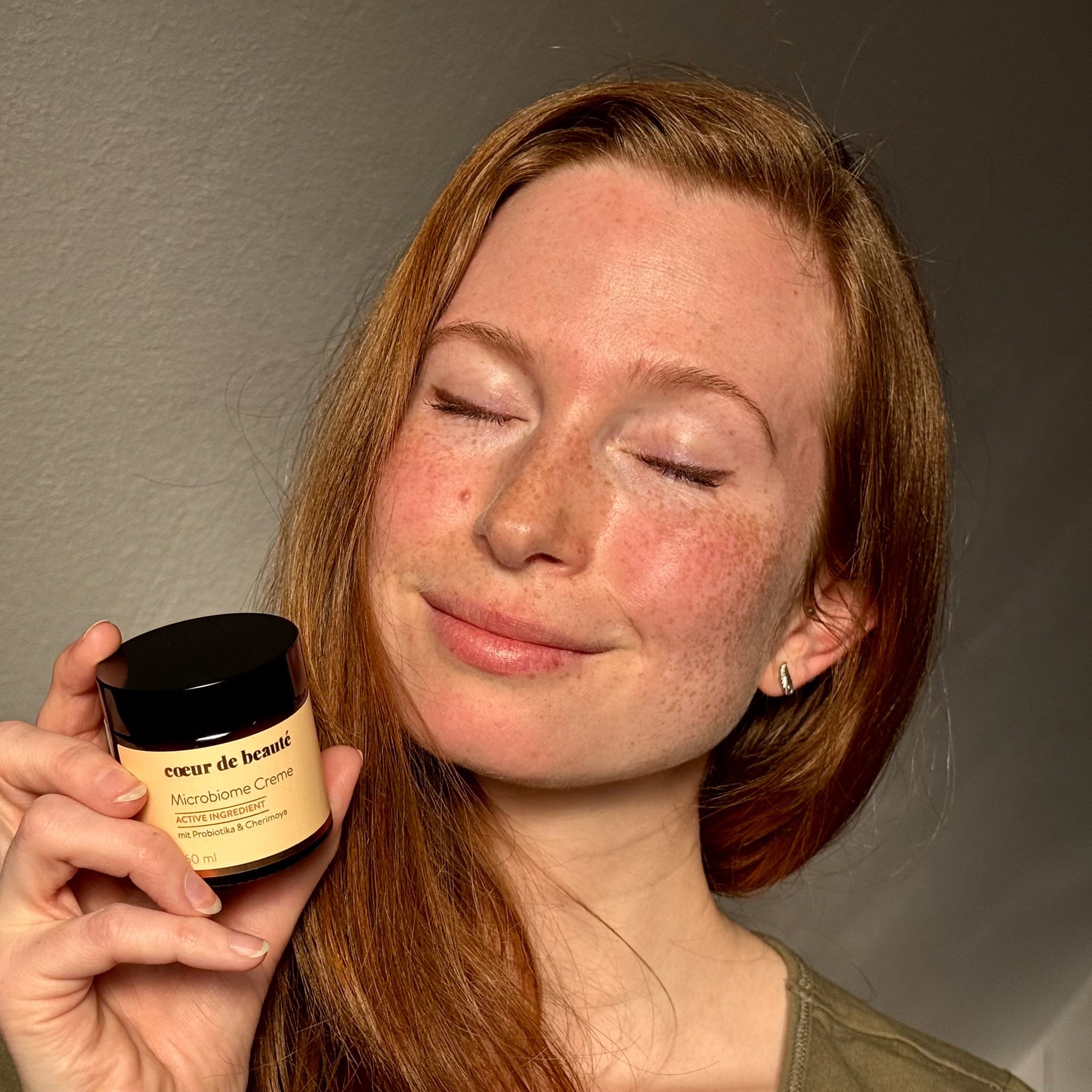 Frau mit lächeln und geschlossenen Augen hält Mikrobiom Creme in der Hand für sensible Haut von coeur de beaute aus Berlin